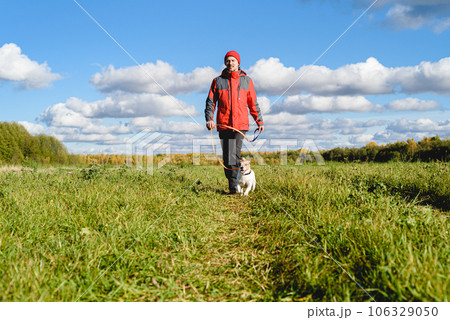 Man and dog on leash walking along path through meadow on bright Fall day 106329050