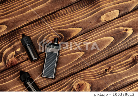 Vape and vape juice bottles on brown wooden background Vape and vape juice bottles on brown wooden background 106329612