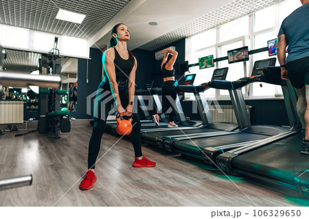 Athletic woman exercising with kettle bell in a gym Athletic woman exercising with kettle bell in a gym 106329650