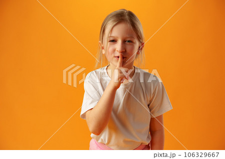 Little girl showing silence gesture against yellow background 106329667