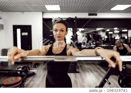 Fit woman doing squats with barbell in a gym 106329781