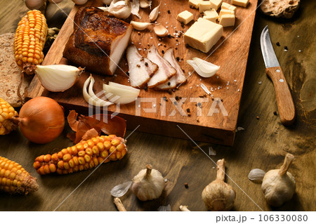 still life of food in a rural style on a dark wood background, sliced lard and garlic, cheese, corn and onion, concept of fresh vegetables and healthy food 106330080