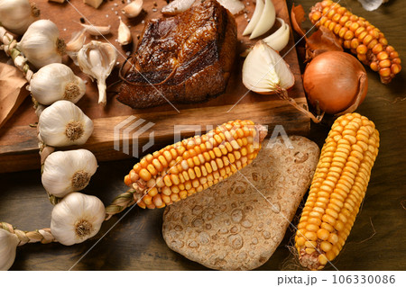 still life of food in a rural style on a dark wood background, sliced lard and garlic, cheese, corn and onion, concept of fresh vegetables and healthy food 106330086