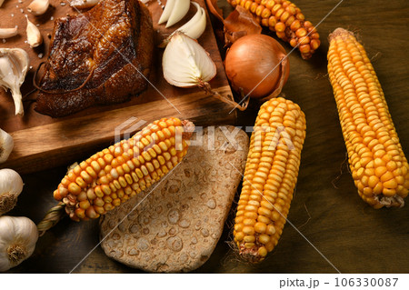 still life of food in a rural style on a dark wood background, sliced lard and garlic, cheese, corn and onion, concept of fresh vegetables and healthy food 106330087