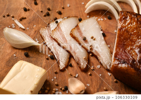 still life of food in a rural style on a dark wood background, sliced cheese and bacon, garlic, salt and pepper, concept of healthy food 106330109