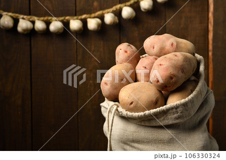 a bag full of potatoes and garlic bulbs, braided like a garland against a dark wood background a bag full of potatoes and garlic bulbs, braided like a garland against a dark wood background 106330324