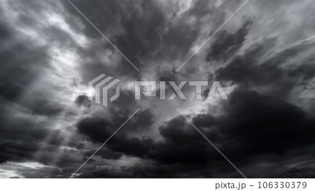 dark dramatic sky with black stormy clouds before rain or snow as abstract background, extreme weather, the sun shines through the clouds, high contrast photo 106330379