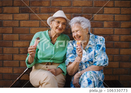 Portrait of two senior female friends in the city, eating ice cream on a hot summer day. 106330773