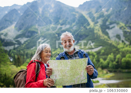 Senior tourists with backpacks reading map, preparing for hike. Senior tourists with backpacks reading map, preparing for hike. 106330860