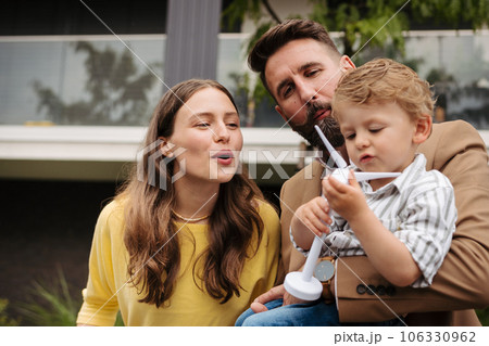 Smiling parents with little son blowing on wind turbine model. 106330962