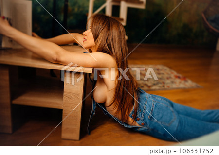 a naked woman in denim jumpsuit lying on the floor near the coffee table 106331752