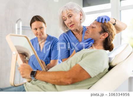 Elderly female cosmetologist consulting man before facial skin treatments Elderly female cosmetologist consulting man before facial skin treatments 106334956