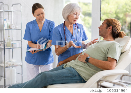 Man sitting in chair and carefully answers mature female doctor questions about well-being 106334964