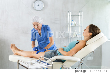 Elderly female doctor performs intra-articular injection treatment of knee bursitis to woman patient 106334974