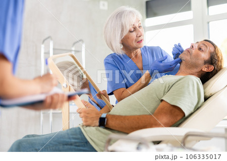 Male patient sitting on examination couch with mirror during consultation of cosmetologist Male patient sitting on examination couch with mirror during consultation of cosmetologist 106335017