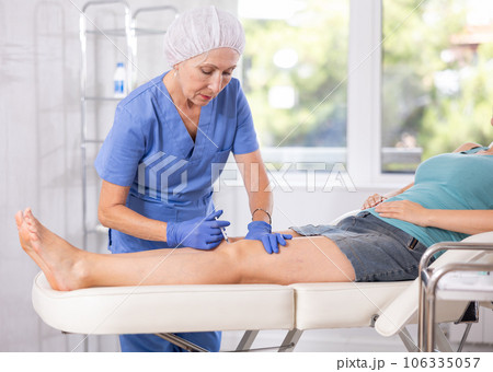 Nurse makes an injection of medicine with a syringe into the sore knee of female patient 106335057