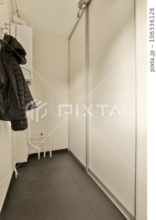 a coat hanging on a wall in a room with white walls and black tile flooring, there is an open door to the 106336126