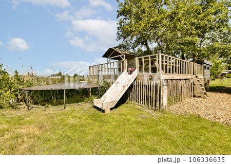 a backyard play area with a slide in the grass and a tree on the other side of the fenced area 106336635