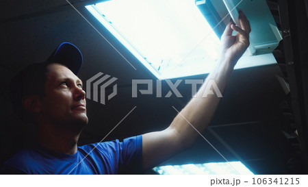 Professional electrician changes fluorescent lamp in ceiling lamp. Worker repairs lighting in office 106341215