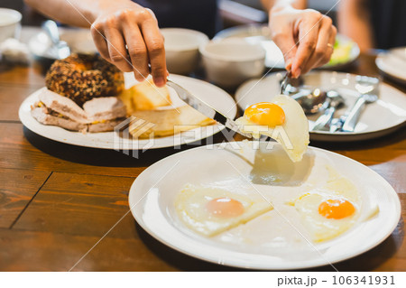 Woman eating fried eggs breakfast with friends on wooden table. Woman eating fried eggs breakfast with friends on wooden table. 106341931