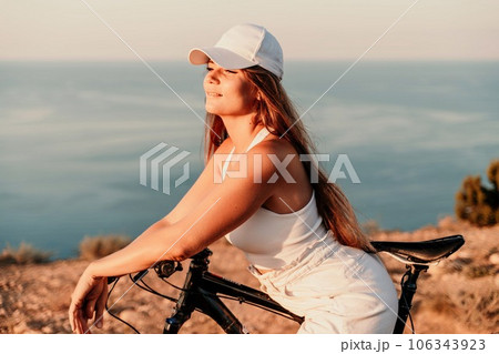 A woman cyclist on a mountain bike looking at the landscape sea. Adventure travel on bike. 106343923