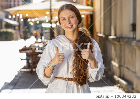 Happy girl showing thumbs up, like sign positive something good positive feedback in city street Happy girl showing thumbs up, like sign positive something good positive feedback in city street 106344232