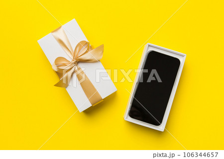 Opened gift box with gold ribbon and smartphone on color background, top view. Blank open box packaging mockup , Template for your design - branding mockup 106344657