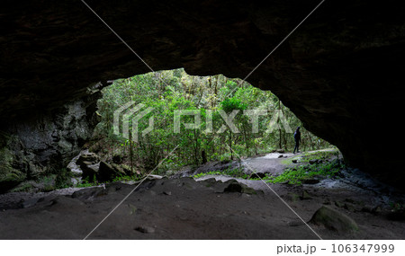 Unidentified Hiker Emerging from Huge Cave into Forest Landscape 106347999