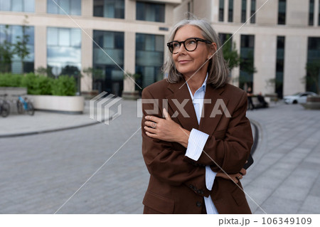 charming successful senior woman with gray hair and glasses is dressed in a brown designer suit charming successful senior woman with gray hair and glasses is dressed in a brown designer suit 106349109