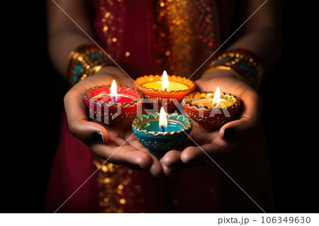 Woman hands with henna holding colorful clay diya lamps lit during diwali celebration 106349630