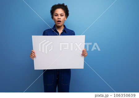 young pretty hispanic business woman with fluffy hair dressed in blue denim suit holding billboard 106350639