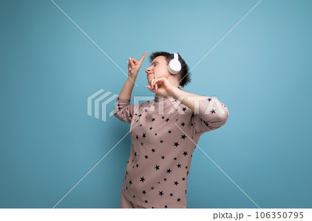 active bright caucasian young woman with a short haircut dressed in a beige suit listens to music in 106350795