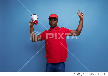 branded clothing concept. american man in red t-shirt and cap reporting news with megaphone branded clothing concept. american man in red t-shirt and cap reporting news with megaphone 106351921
