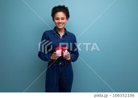 a slender young hispanic brunette woman with fluffy curly hair in a blue denim suit hugging a gift 106352106