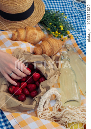 Enjoying a picnic: croissants, strawberries, lemonade on checkered blanket Enjoying a picnic: croissants, strawberries, lemonade on checkered blanket 106352829