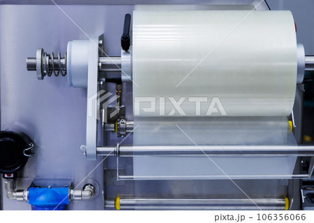 roll of plastic packaging film on the automatic packing machine in food product factory. industrial and technology concept. roll of plastic packaging film on the automatic packing machine in food product factory. industrial and technology concept. 106356066