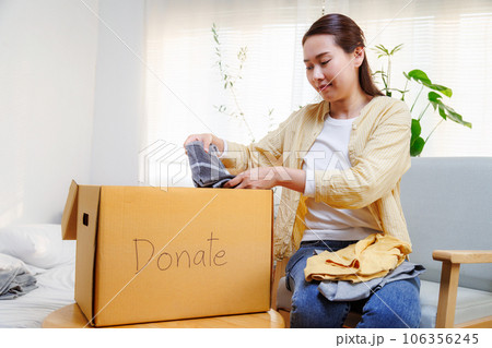 volunteer asian woman putting unused clothes into cardboard boxes for donation and charity. Reuse, recycle, renewable and sustainability concept. 106356245