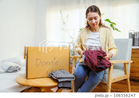 volunteer asian woman putting unused clothes into cardboard boxes for donation and charity. Reuse, recycle, renewable and sustainability concept. volunteer asian woman putting unused clothes into cardboard boxes for donation and charity. Reuse, recycle, renewable and sustainability concept. 106356247