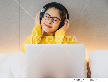 Asian woman enjoying listening music in headphones while quarantine herself at home. Conceptual of woman lifestyle. Asian woman enjoying listening music in headphones while quarantine herself at home. Conceptual of woman lifestyle. 106356290