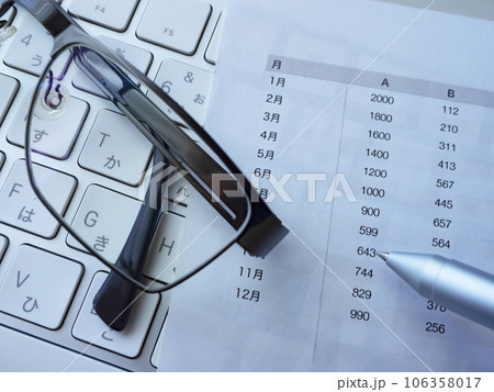 テーブルに置かれた書類とメガネとキーボード 106358017