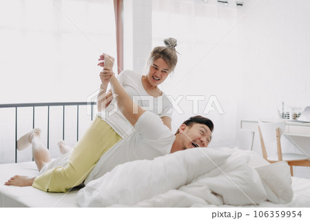 Funny couple wife giving husband hurt massage in white bedroom. Funny couple wife giving husband hurt massage in white bedroom. 106359954