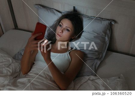 Young woman surfing the Internet with her smartphone in bed at night. Young woman surfing the Internet with her smartphone in bed at night. 106360520