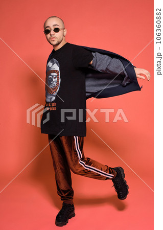 Studio shot of a young tattoed bald man posing against a pink background. 90s style. 106360882