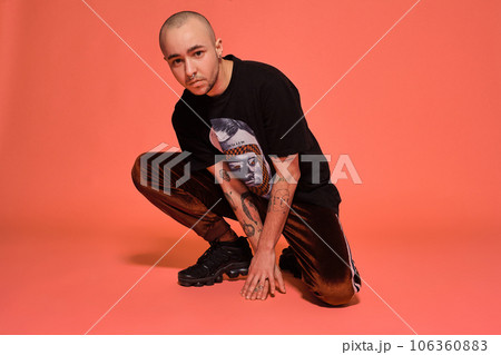 Studio shot of a young tattoed bald man posing against a pink background. 90s style. 106360883