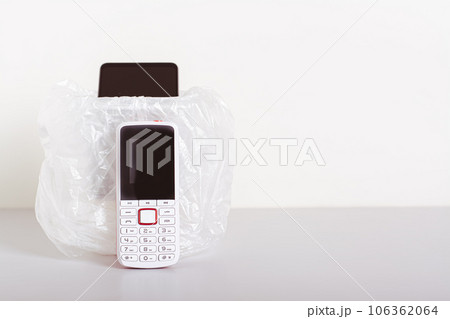 A white push-button telephone stands by the trash can with a smartphone on the table 106362064