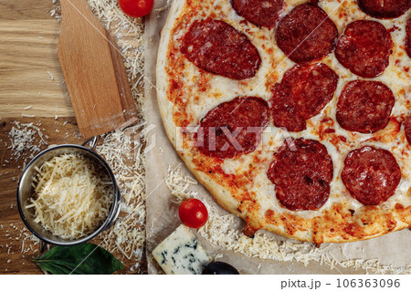 Pizza with chicken cheese and pepperoni, a piece of which is cut and laid out like a pakman, is on a wooden board and a brown background. Cheese spreads flowing streaks Pizza with chicken cheese and pepperoni, a piece of which is cut and laid out like a pakman, is on a wooden board and a brown background. Cheese spreads flowing streaks 106363096