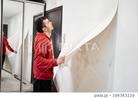 Repair the house with their own hands. The guy is ripping the old wallpaper off the wall 106363220
