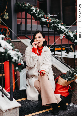 beautiful brunette eats chocolate on the stairs with shopping. winter city 106363329