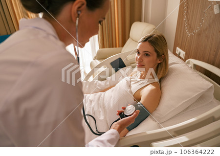 Doctor checking blood pressure of young woman patient in ward of modern clinic Doctor checking blood pressure of young woman patient in ward of modern clinic 106364222