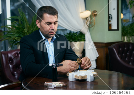 Man cutting cigar before smoking while sitting in a restaurant Man cutting cigar before smoking while sitting in a restaurant 106364362